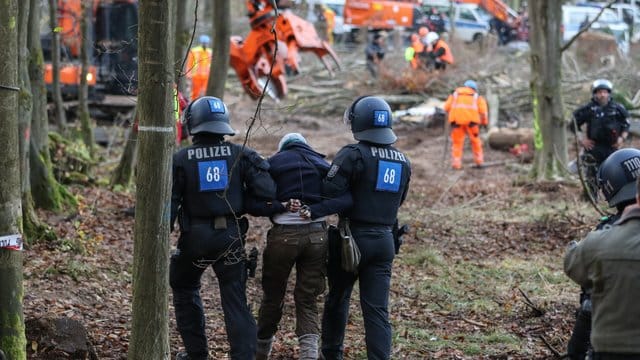 Polizisten führen eine A49-Gegnerin durch ein bereits gerodetes Waldgebiet.