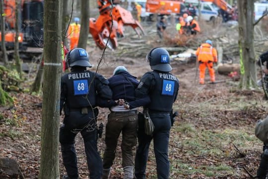 Polizisten führen eine A49-Gegnerin durch ein bereits gerodetes Waldgebiet.