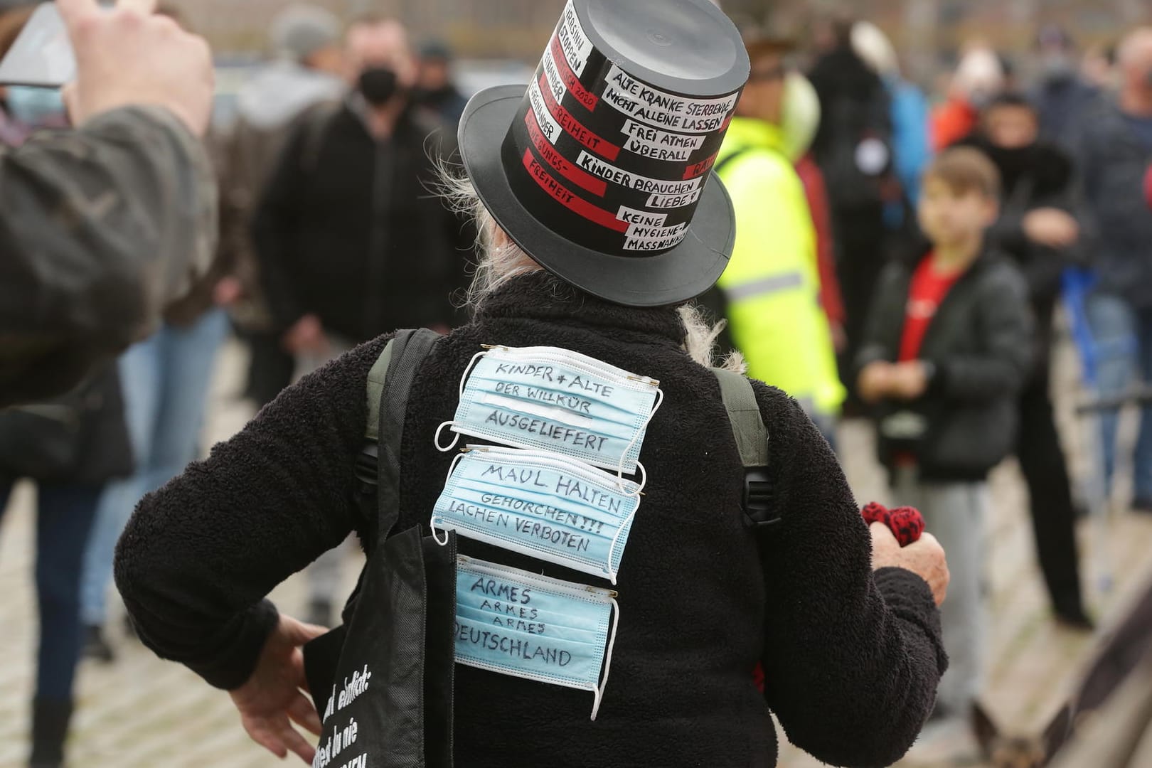 Mund-Nase-Masken mit Slogans gegen die Corona-Maßnahmen sind auf der Jacke einer Frau befestigt, die an einer Demonstration der Initiative «Querdenken 211» teilnimmt: Zu der Kundgebung kamen weniger Menschen als erwartet.