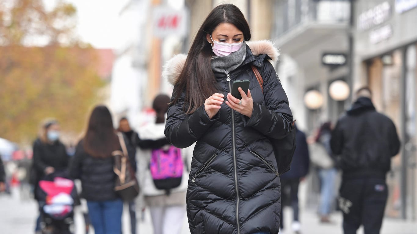 Eine Frau mit Mund-Nasen-Schutz schaut auf ihr Smartphone: Düsseldorfer können in dem neuen Supermarkt kontaktlos einkaufen.