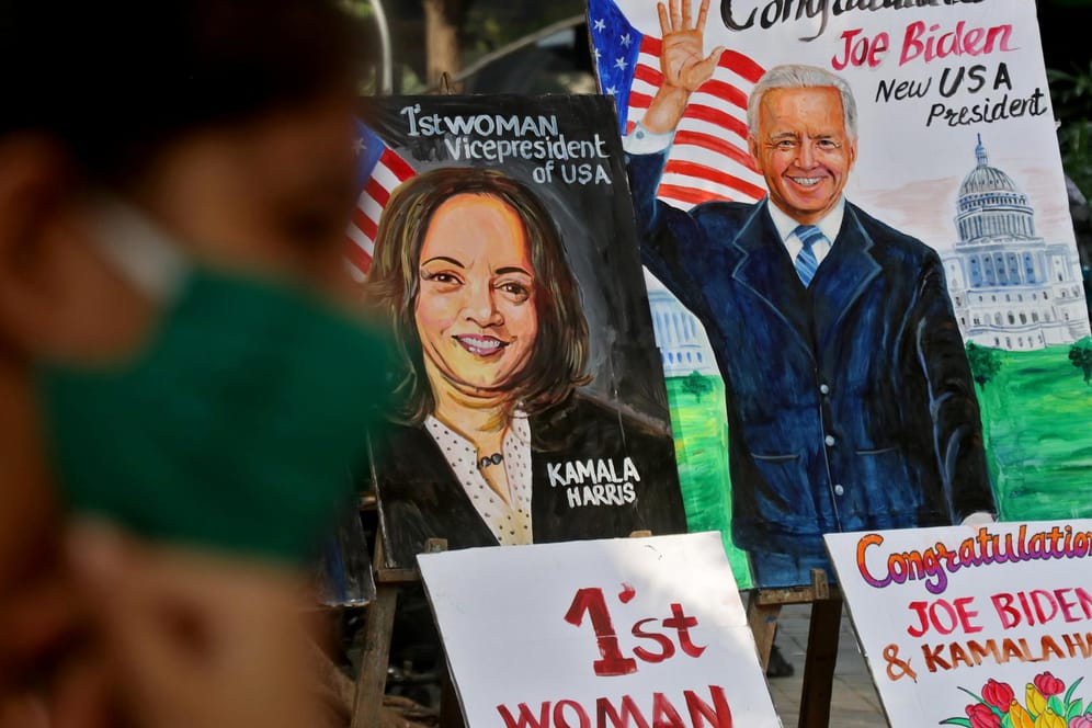 Weltereignis: In Mumbai in Indien bietet ein Händler Zeichnungen von den Siegern der US-Präsidentschaftswahl, Joe Biden und Kamala Harris, an, während im Vordergrund ein Mädchen mit Mund-Nase-Schutz sitzt.