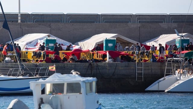 Migranten stehen an der Mole der Hafenstadt Arguineguín im Südwesten von Gran Canaria. Migranten stehen an der Mole der Hafenstadt Arguineguín im Südwesten von Gran Canaria.