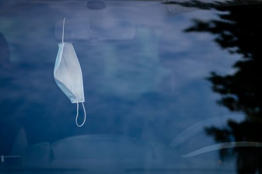 Eine Mund-Nasen-Bedeckung hängt in einem geparkten Auto in Berlin.