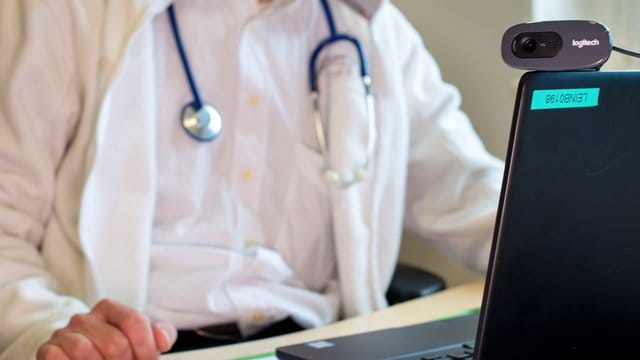 Ein Hausarzt sitzt während einer Videosprechstunde in seiner Praxis vor einem Laptop. Ein Hausarzt sitzt während einer Videosprechstunde in seiner Praxis vor einem Laptop.