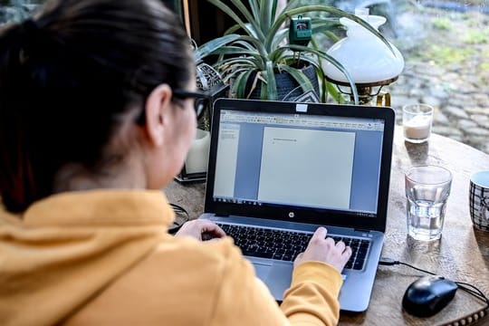 Eine junge Frau arbeitet im Homeoffice in einem Wintergarten.
