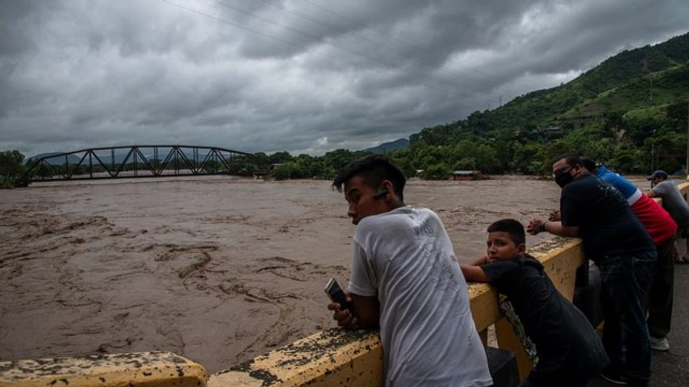 Menschen stehen auf einer Brücke und beobachten wie der Fluss Chamalecon in Honduras über die Ufer tritt.