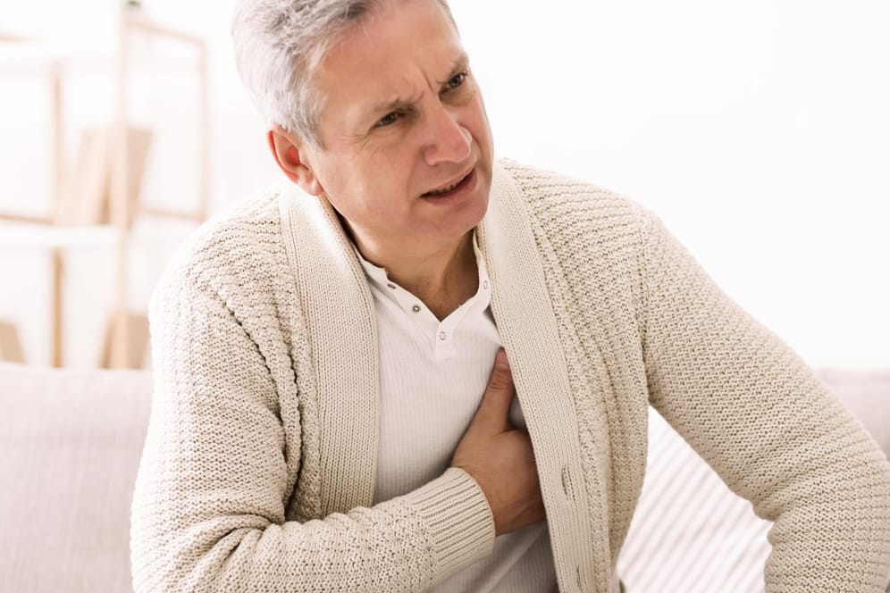 Mann hat Brustschmerzen und fasst sich an die Brust: Schmerzen in der Brust und Fieber können auf eine Herzbeutelentzündung hindeuten