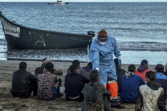 Migranten aus Marokko lassen ihre Temperatur messen, nachdem sie mit einem Holzboot an der Küste von Gran Canaria angekommen sind.