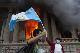 Ein Demonstrant schwenkt vor dem brennenden Kongress die Nationalfahne.
