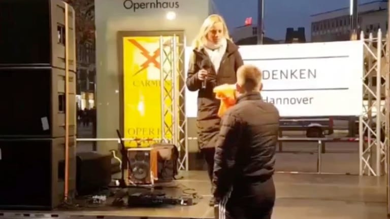 Ein Mann drückt einer Rednerin auf einer "Querdenken"-Demonstration eine Warnweste in die Hand: Sie hatte sich zuvor mit Sophie Scholl verglichen.