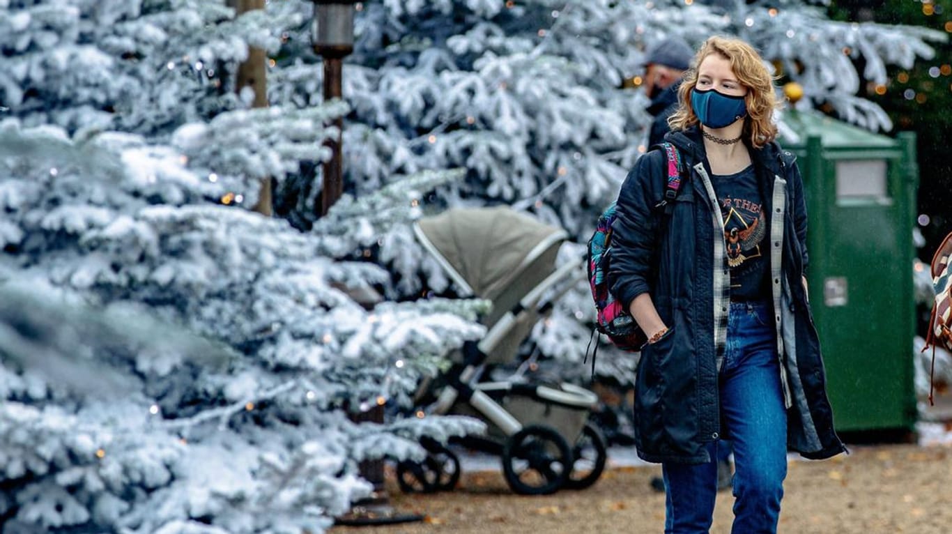 Ein Frau mit Maske betrachtet in den Niederlanden weihnachtlich dekorierte Tannenbäume: Auch bei einem Lockdown sollten Sie im Corona-Winter in Bewegung bleiben.
