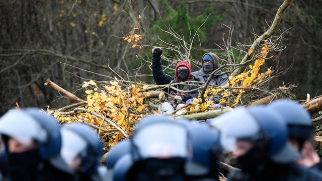 Zwei Aktivisten sitzen am Dannenröder Forst auf einem Stapel gerodeter Bäume vor einer kette Polizisten (Archivbild): Mit den Aktivisten solidarisierten sich einige Baumbesetzer in Köln.