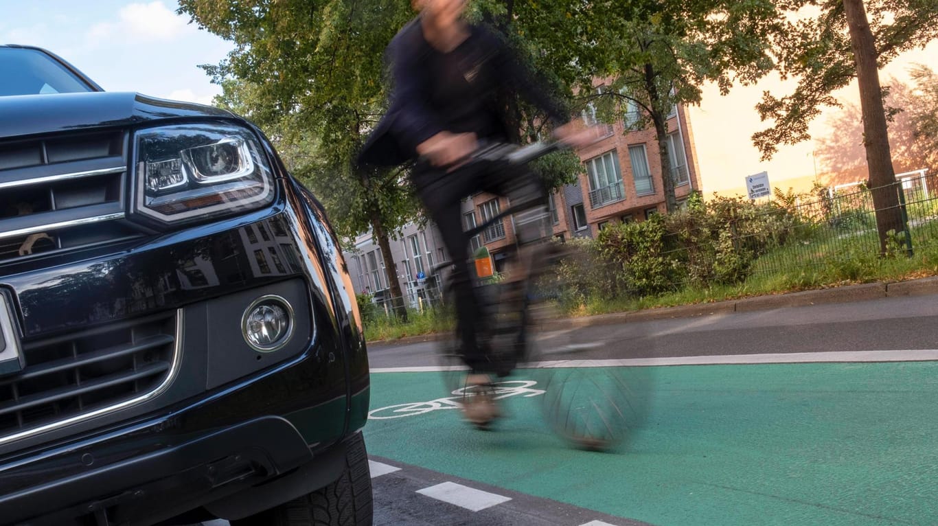 Eine Autofront bewegt sich nahe eines Radfahrers (Symbolbild): In Köln ist es zu einem Unfall zwischen einem Auto und einem Radfahrer gekommen.