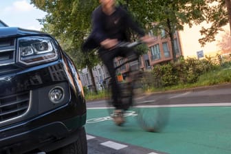 Eine Autofront bewegt sich nahe eines Radfahrers (Symbolbild): In Köln ist es zu einem Unfall zwischen einem Auto und einem Radfahrer gekommen.