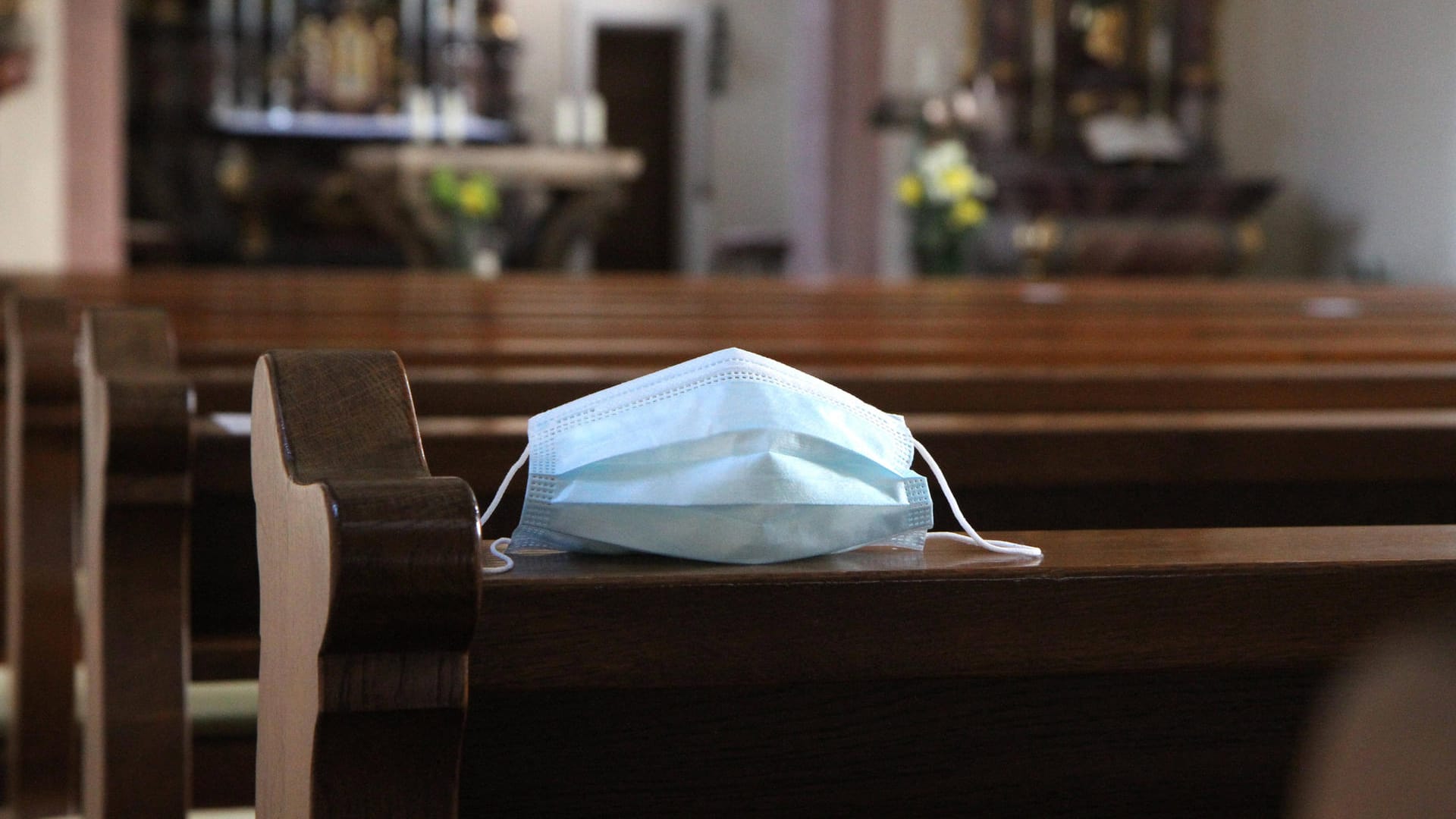 Eine Mund-Nasen-Maske liegt auf einer Kirchenbank (Symbolbild): In Wuppertal und anderen Städten in NRW bereiten sich die Kirchen auf besondere Corona-Gottesdienste zu Weihnachten vor.