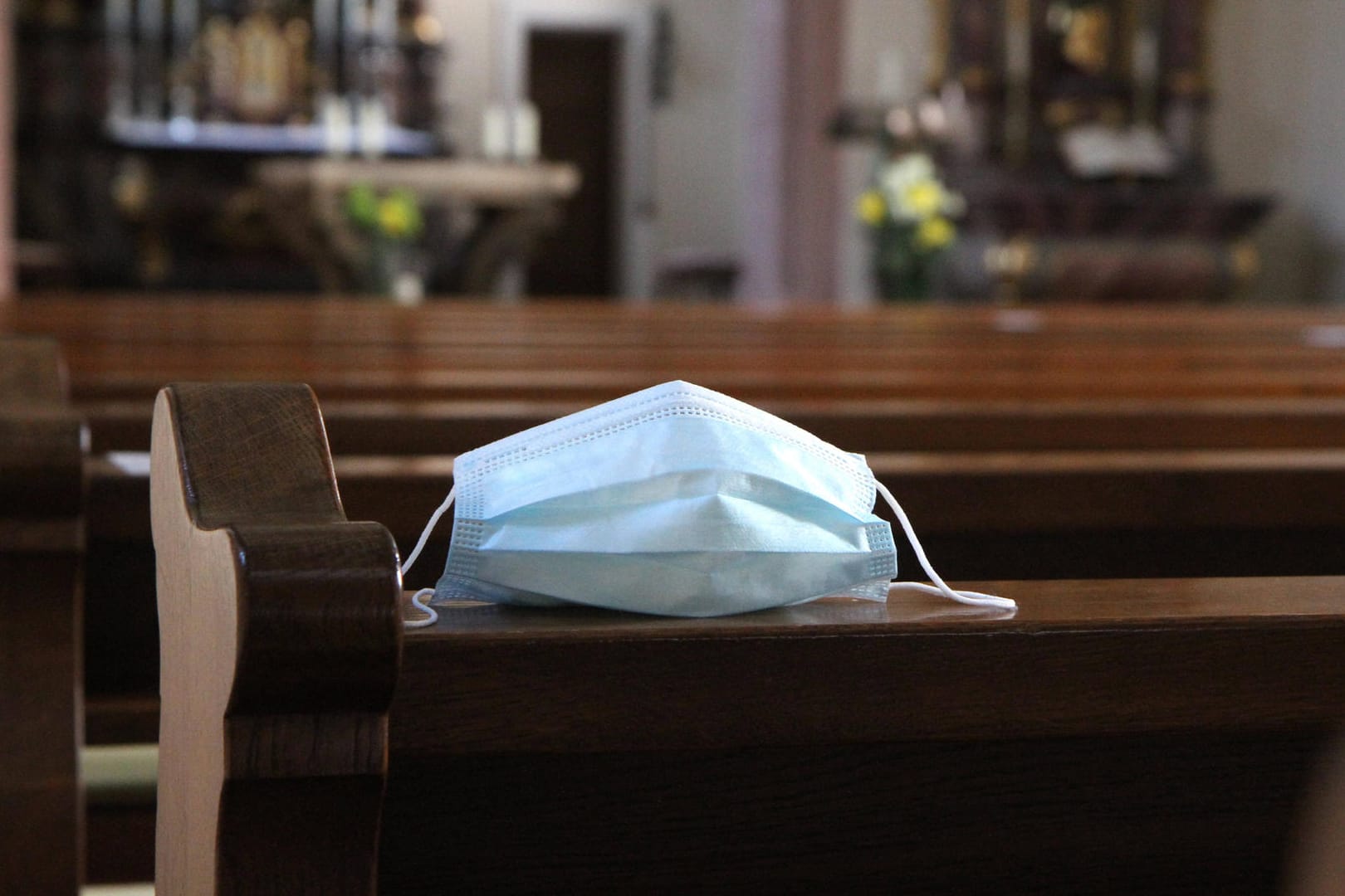 Eine Mund-Nasen-Maske liegt auf einer Kirchenbank (Symbolbild): In Wuppertal und anderen Städten in NRW bereiten sich die Kirchen auf besondere Corona-Gottesdienste zu Weihnachten vor.