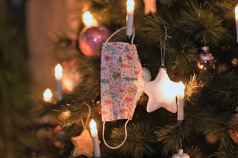 Ein Mund-Nasen-Schutz hängt an einem Weihnachtsbaum (Symbolbild): Wegen Corona fällt das Weihnachtsfest dieses Jahr anders aus, der Barmer Kulturadvent hat sich dennoch etwas einfallen lassen, um Stimmung zu verbreiten.