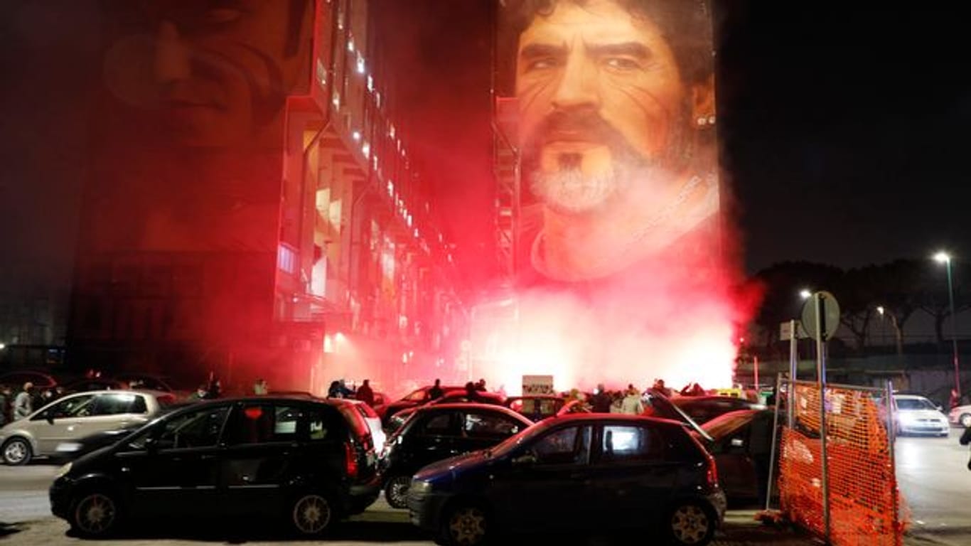 Trauernde sammeln sich unter einem Wandgemälde des Straßenkünstlers Jorit mit der Darstellung von Diego Maradona und zünden Leuchtfackeln an.