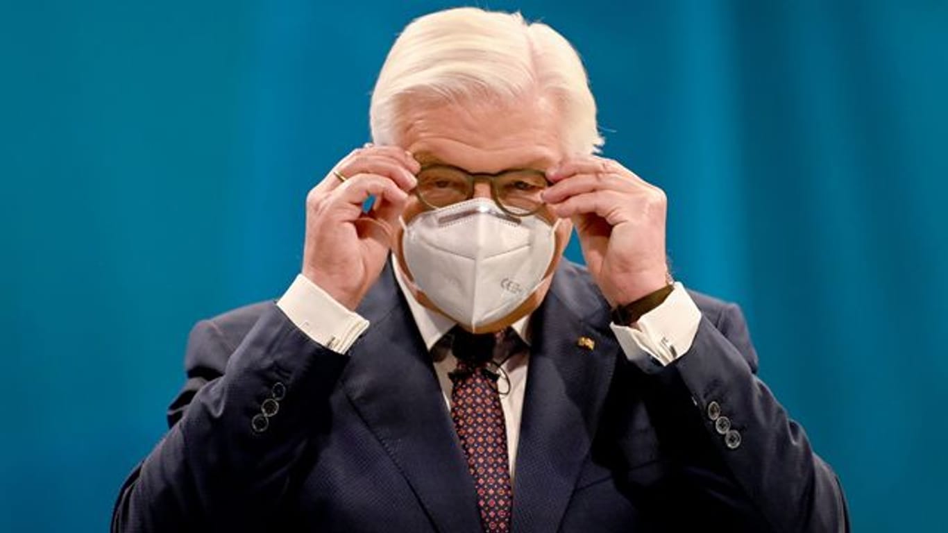 Bundespräsident Frank-Walter Steinmeier setzt sich einen Mund-Nasen-Schutz auf.
