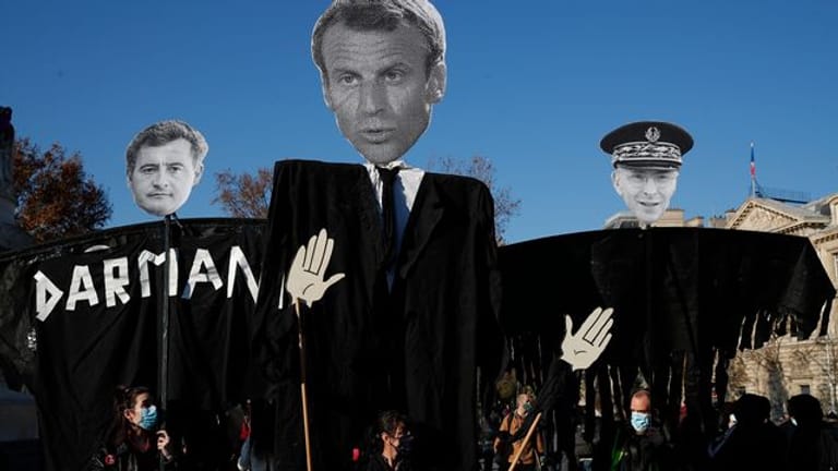 Die Abbilder des französischen Innenministers Darmanin (l-r), des französischen Präsidenten Macron und des Pariser Polizeipräfekten Lallement werden während einer Demonstration gegen ein neues Sicherheitsgesetz in die Höhe gehalten.