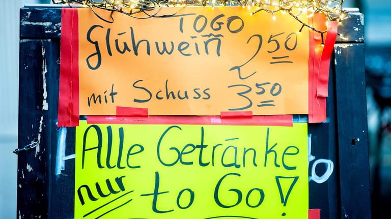 Ein Schild mit der Aufschrift "Glühwein mit Schuss" und dem Hinweis "To-Go" steht vor einer Bar (Symbolbild): In Köln häufen sich die Beschwerden über zu viele Leute vor Glühweinständen.