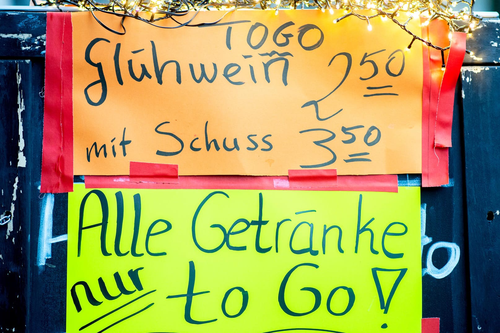 Ein Schild mit der Aufschrift "Glühwein mit Schuss" und dem Hinweis "To-Go" steht vor einer Bar (Symbolbild): In Köln häufen sich die Beschwerden über zu viele Leute vor Glühweinständen.