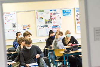 Schüler einer Klasse sitzen mit Mund-Nasen-Bedeckungen im Unterricht (Symbolbild): Für Schüler und Lehrer sind die Lern- und Arbeitsbedingungen wegen der Corona-Regeln schwieriger geworden.