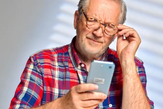 Ein Mann schaut skeptisch auf sein Handy: Wir klären über aktuelle Betrugsversuche per Telefon, Mail oder Kurznachricht auf.