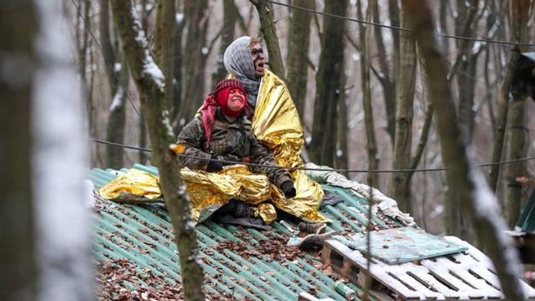 Zwei Umweltaktivisten sitzen in Überlebensdecken gehüllt auf einem Baumhaus im Wald.