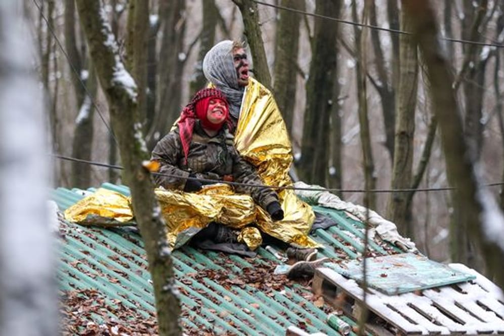 Zwei Umweltaktivisten sitzen in Überlebensdecken gehüllt auf einem Baumhaus im Wald.