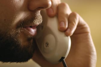 Ein Mann spricht in einen Telefonhörer: Die Bundesnetzagentur geht gegen betrügerische Geschäftsmodelle mit Callcentern vor.