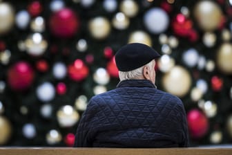 Ein Mann sitzt allein auf einer Bank vor einem geschmückten Weihnachtsbaum: Senioren haben Angst Weihnachten allein zu verbringen.