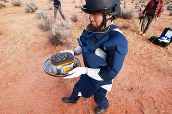 Ein Wissenschaftler hält in der Wüste des Woomera-Testgeländes für Luft- und Raumfahrt im Süden Australiens die Probenkapsel der japanischen Raumsonde "Hayabusa2".