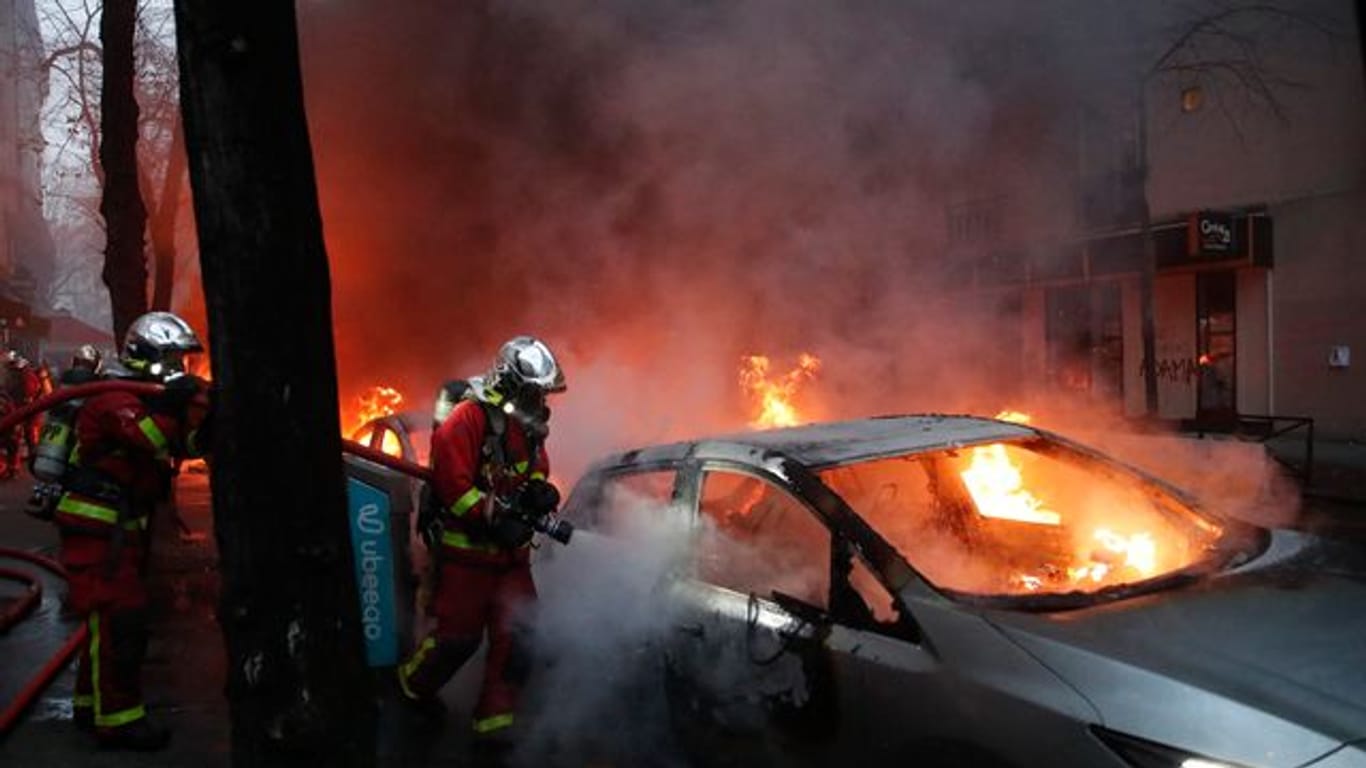 Feuerwehrleute löschen während eines Protestes auf einer Straße ein brennendes Auto.