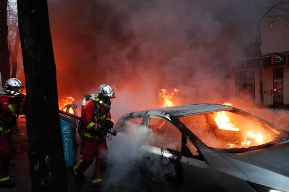 Feuerwehrleute löschen während eines Protestes auf einer Straße ein brennendes Auto.