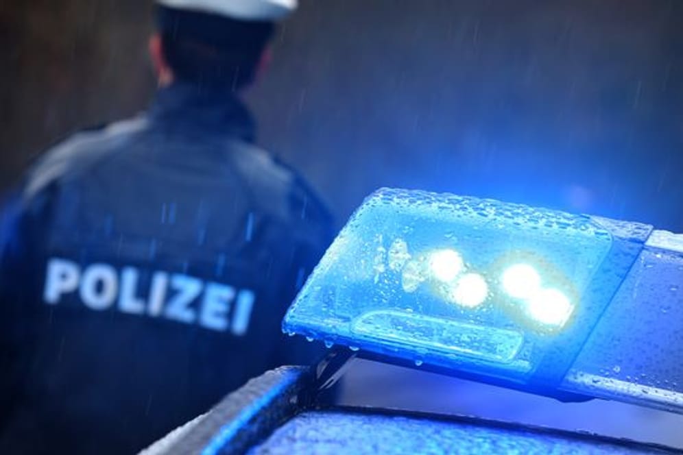 Ein Polizist steht im Regen vor einem Streifenwagen mit Blaulicht (Symbolbild): In Hamburg haben rund 1.300 Polizisten einen Nebenjob.