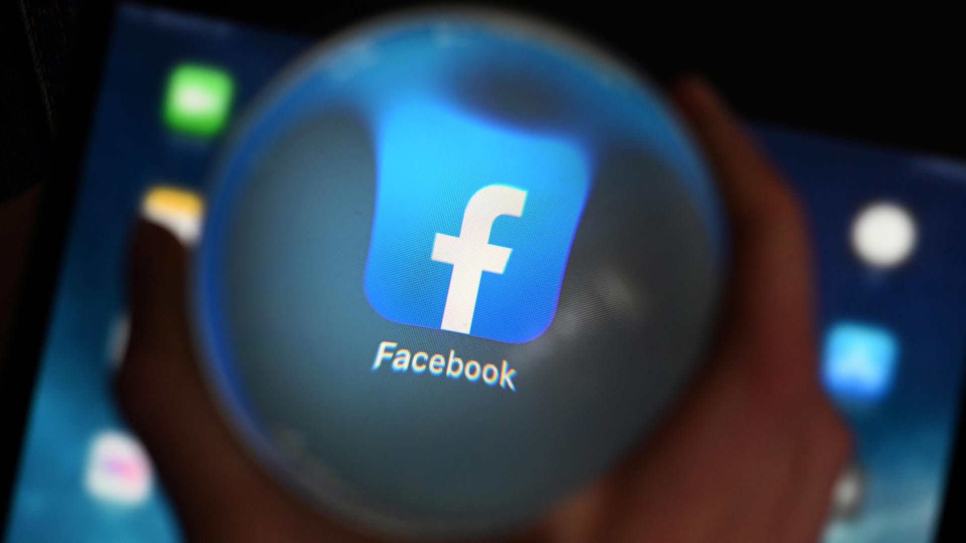Eine Person schaut durch eine Glaskugel auf einem Tablet auf die Facebook App: In dem Netzwerk sollen sich die Mitglieder mit ihrem Klarnamen anmelden. Eine Person schaut durch eine Glaskugel auf einem Tablet auf die Facebook App: In dem Netzwerk sollen sich die Mitglieder mit ihrem Klarnamen anmelden.