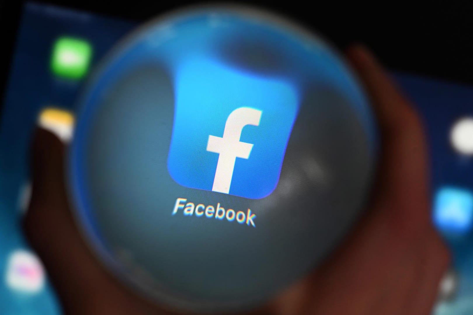 Eine Person schaut durch eine Glaskugel auf einem Tablet auf die Facebook App: In dem Netzwerk sollen sich die Mitglieder mit ihrem Klarnamen anmelden.