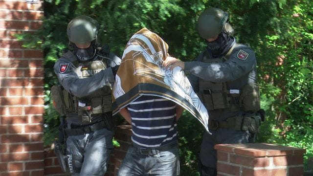 Polizisten führen einen Verdächtigen in Handschellen ab. Polizisten führen einen Verdächtigen in Handschellen ab.