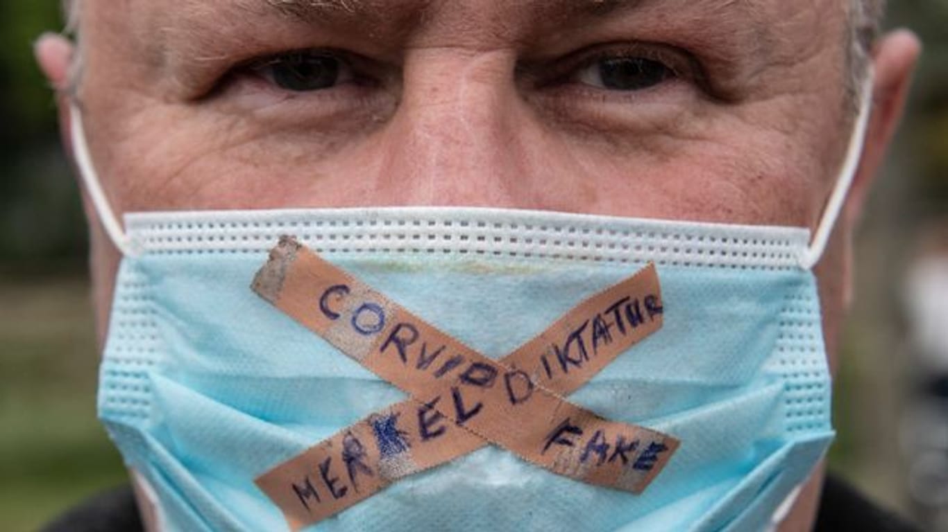 Ein Teilnehmer einer Kundgebung gegen die Corona-Maßnahmen der Regierung trägt einen Mundschutz mit der Aufschrift "Merkel-Diktatur - Covid-Fake".