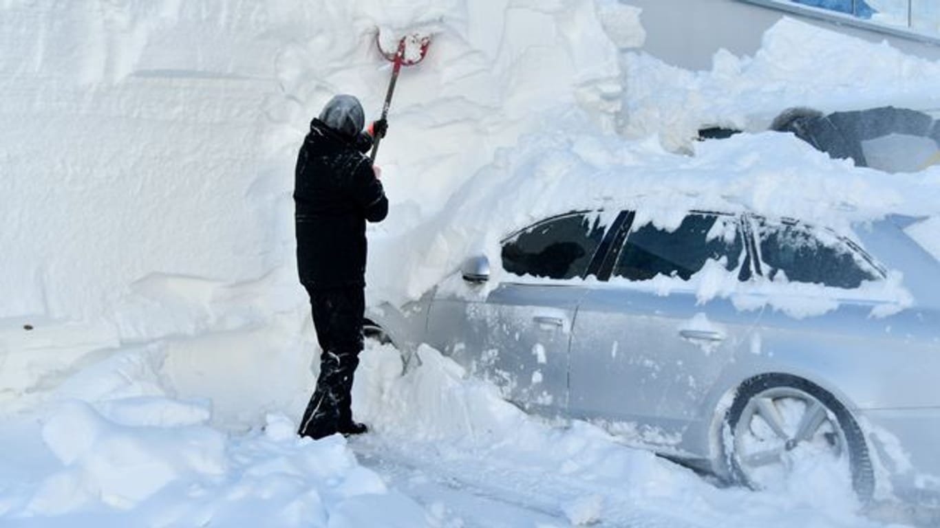 Ein Mann befreit ein eingeschneites Auto von den Schneemengen