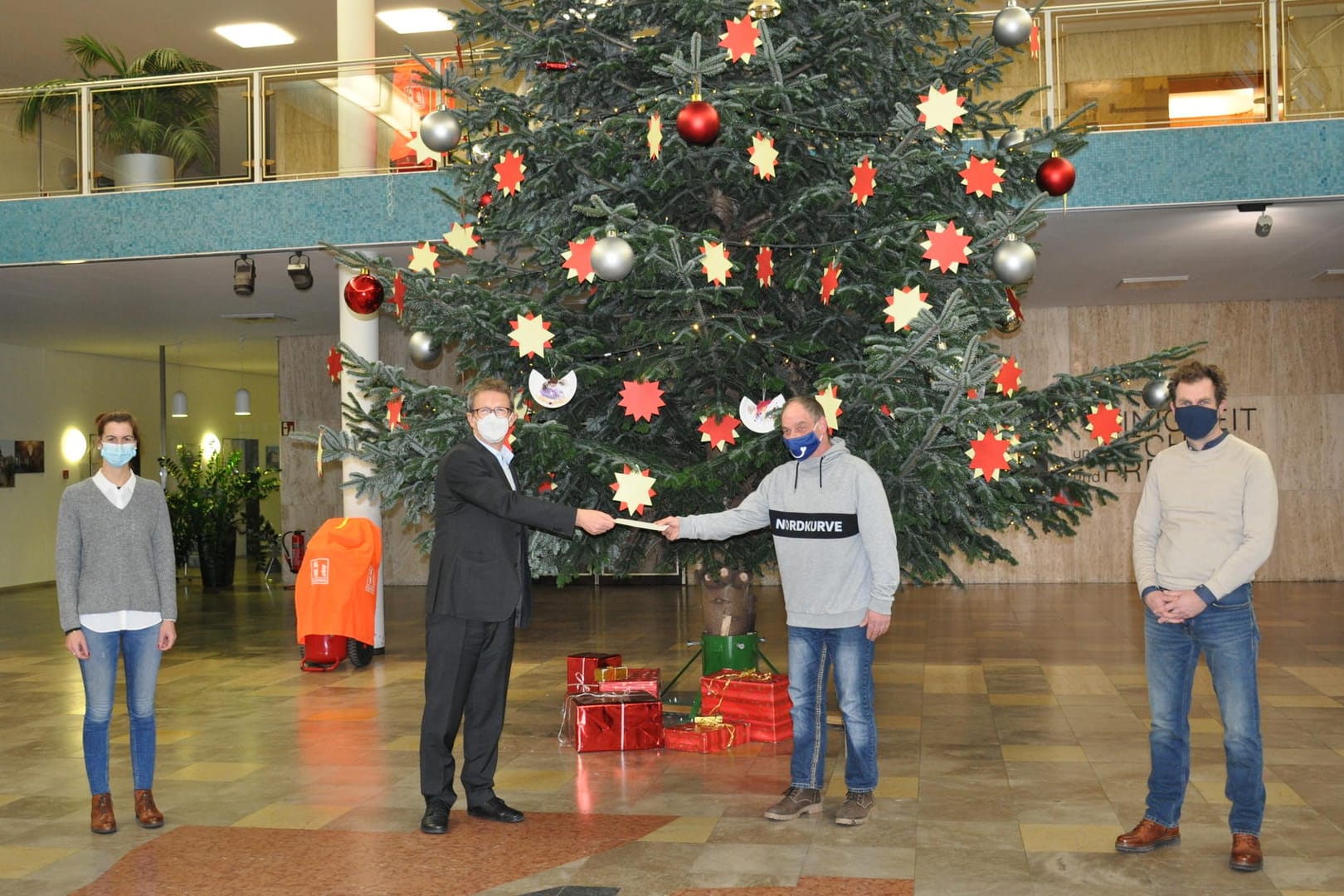 Jasmin Hinze, Klaus Mohrs, Thomas Krücker und Michael Bahn (von links) vor dem Weihnachtsbaum in der Bürgerhalle: OB Mohrs überreichte dem Tagestreff "Carpe Diem" eine Spende.