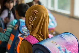 Das Symbolfoto zeigt ein Mädchen mit Kopftuch vor einem Klassenzimmer.