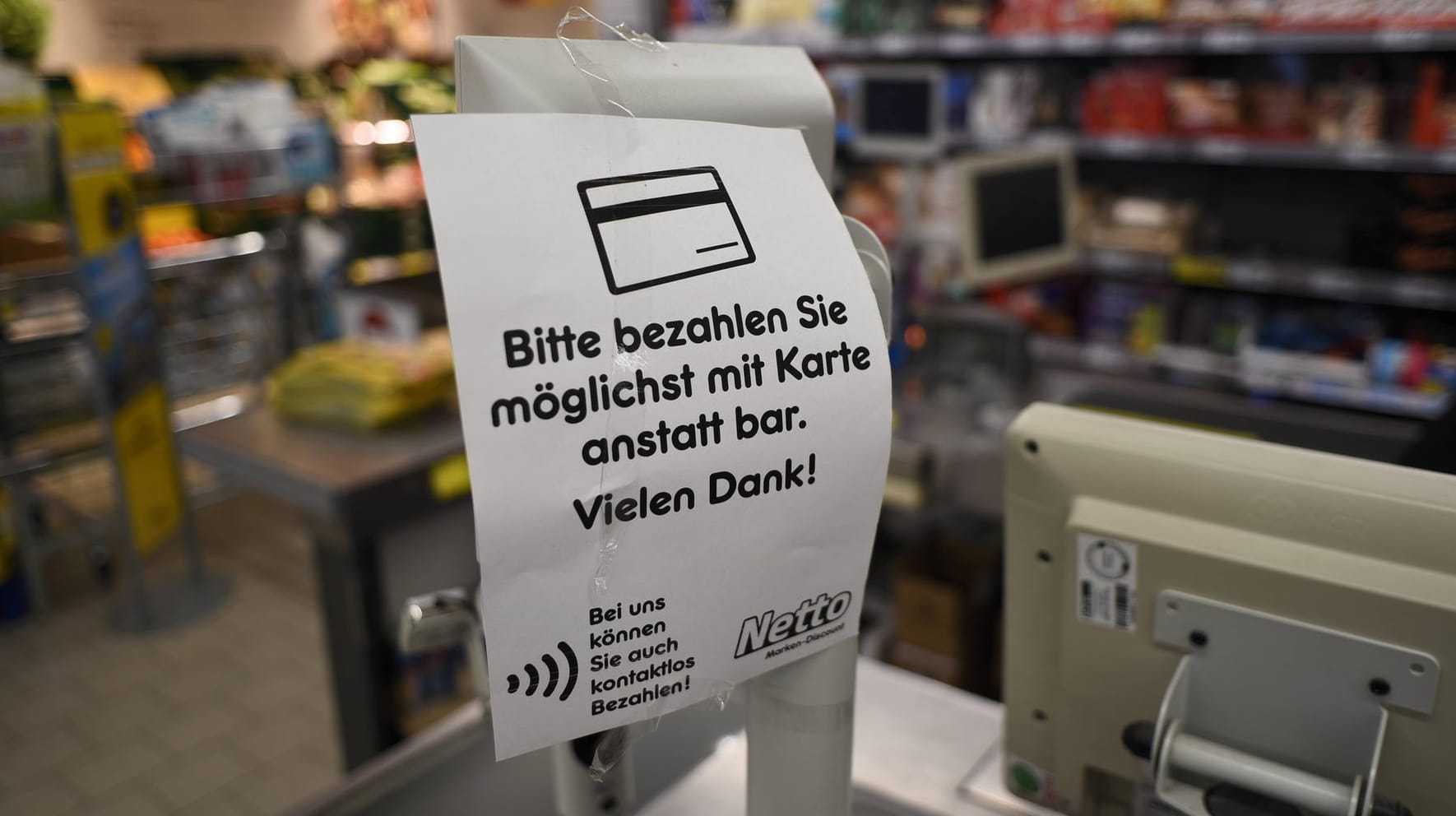 Auf einem Zettel in einem Discounter steht "Bitte bezahlen Sie möglichst mit Karte anstatt bar."