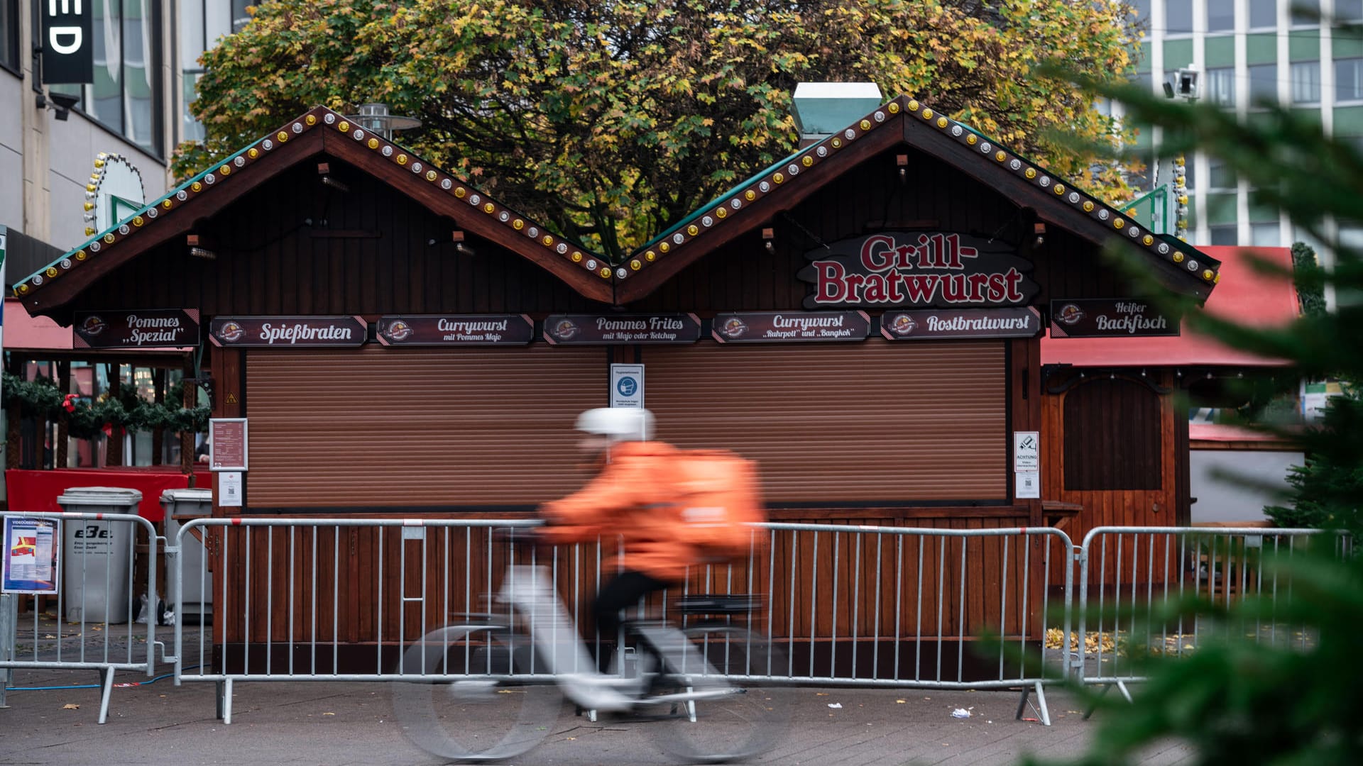 Ein Fahrradfahrer eines Lieferdienst fährt an einer Bude für Grill- und Bratwurst des Weihnachtsmarkt in der Essener Innenstadt vorbei.