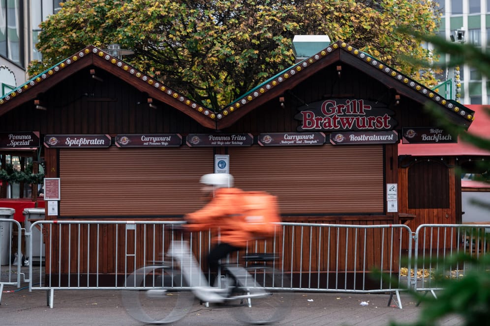 Ein Fahrradfahrer eines Lieferdienst fährt an einer Bude für Grill- und Bratwurst des Weihnachtsmarkt in der Essener Innenstadt vorbei.