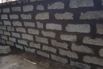 Eine Mauer aus Bausteinen, die zum Teil aus desinfizierten und geschredderten Masken und Schutzanzügen besteht.