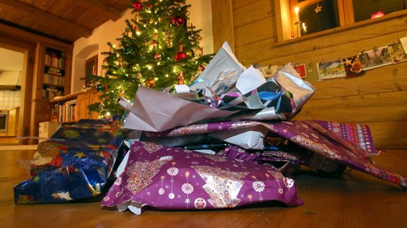 Zerknülltes weihnachtliches Geschenkpapier liegt vor einem geschmücktem Christbaum.
