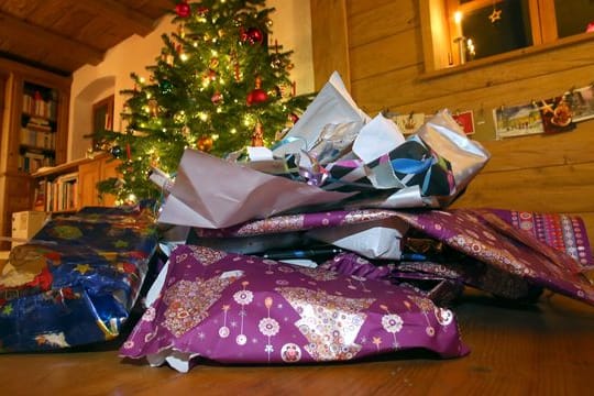 Zerknülltes weihnachtliches Geschenkpapier liegt vor einem geschmücktem Christbaum.