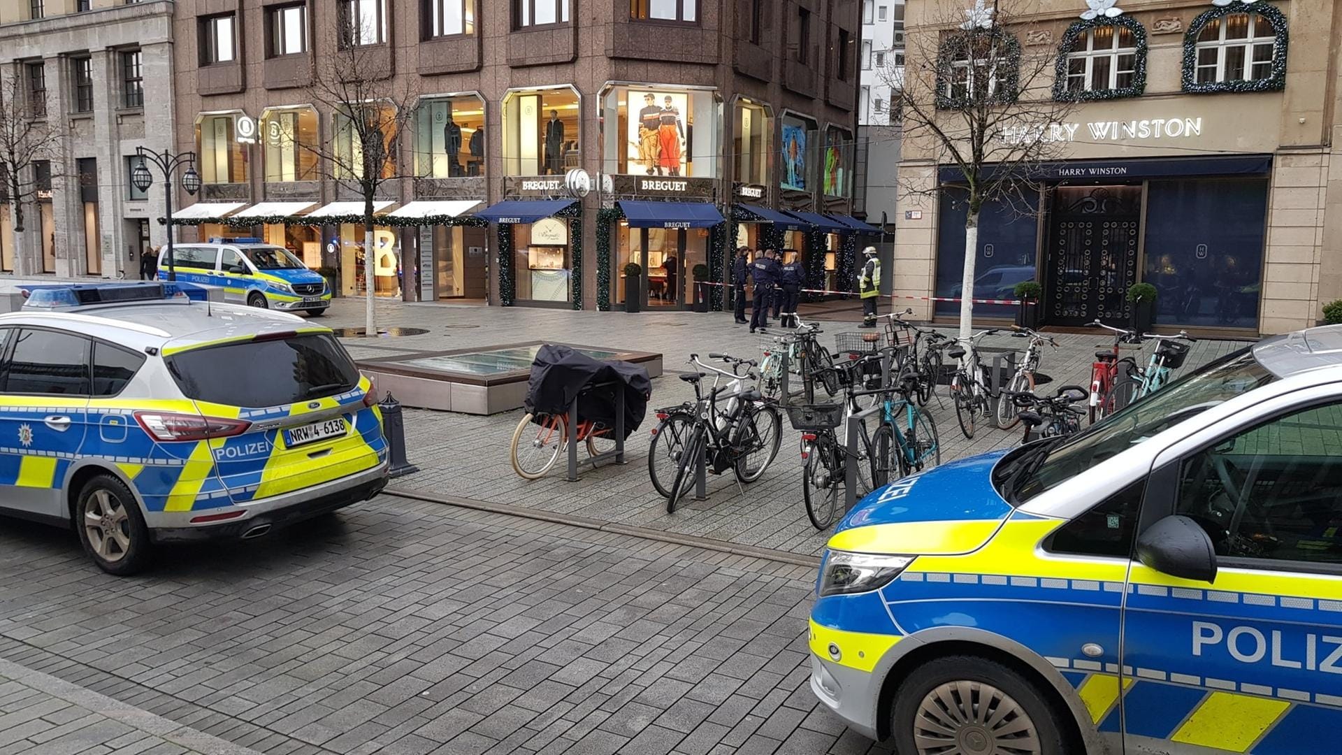 Polizisten stehen auf der Königsallee in der Nähe eines Juweliergeschäfts, das zuvor von mehreren Tätern überfallen worden war: Die Täter sind flüchtig.